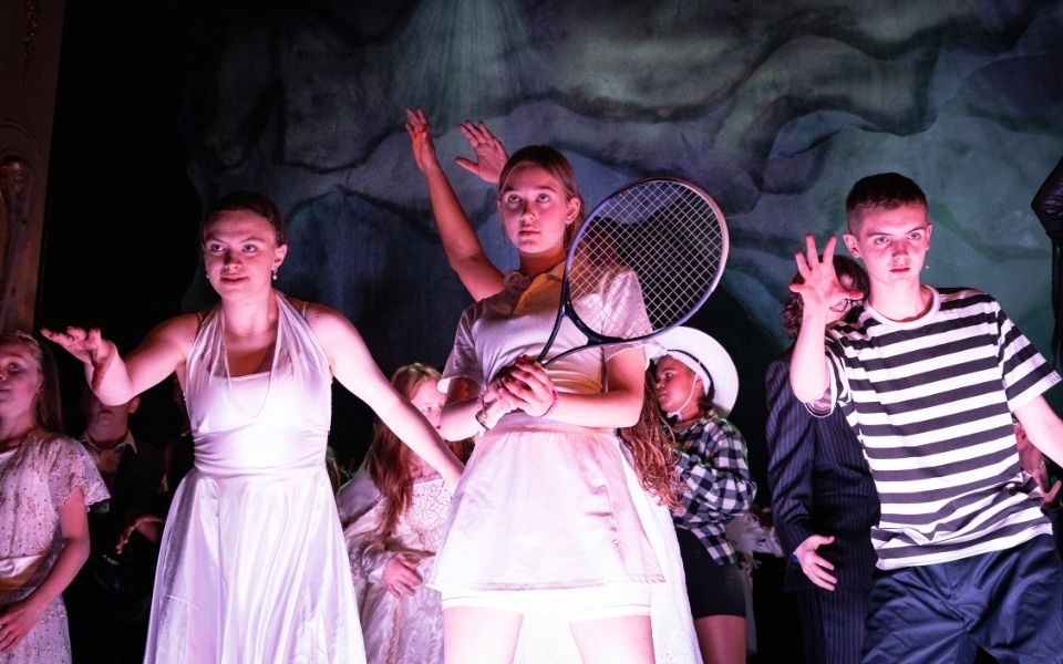 In an ensemble striking poses, a young person stands holding a tennis racket