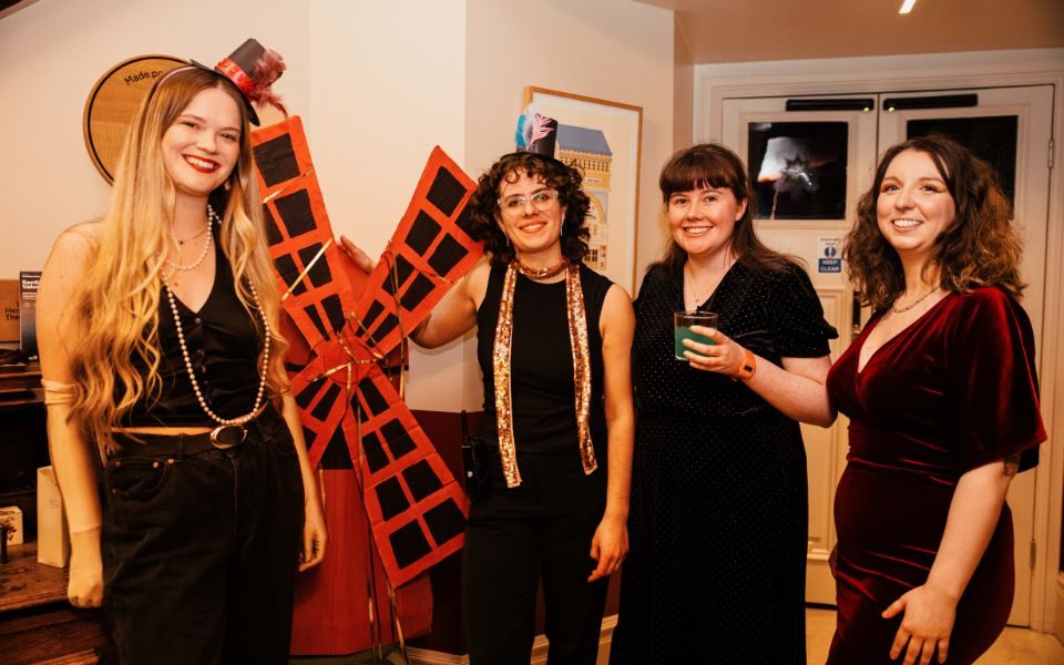Four people posing in the foyer of Hyde Park Picture House with a cardboard recreation of the Moulin Rouge windmill