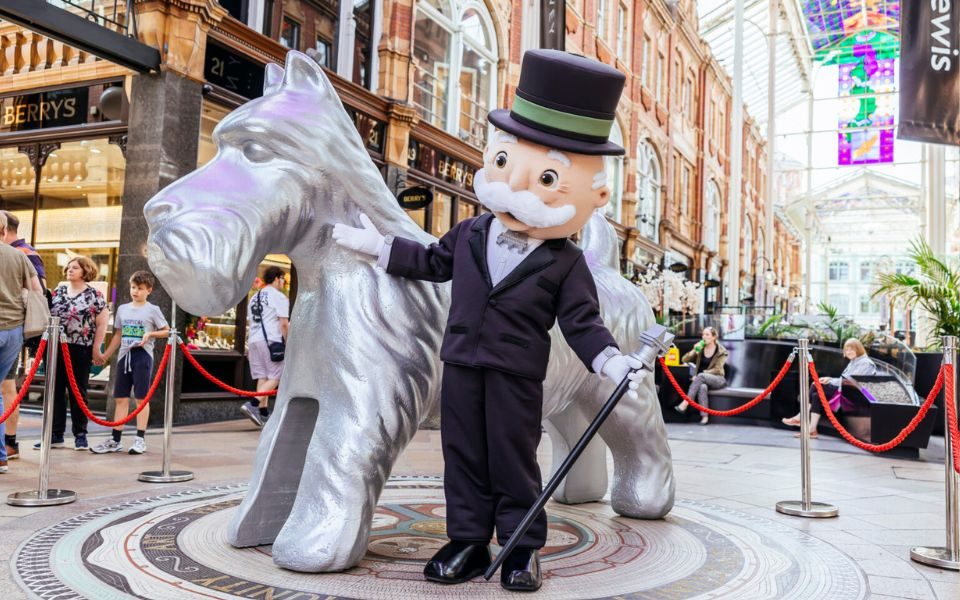 A giant silver scotty dog based on the Monopoly game piece next to a lifesize figure of the Monopoly man, wearing a suit and top hat with a white moustache and monocle, holding a cane in his white gloved hand.