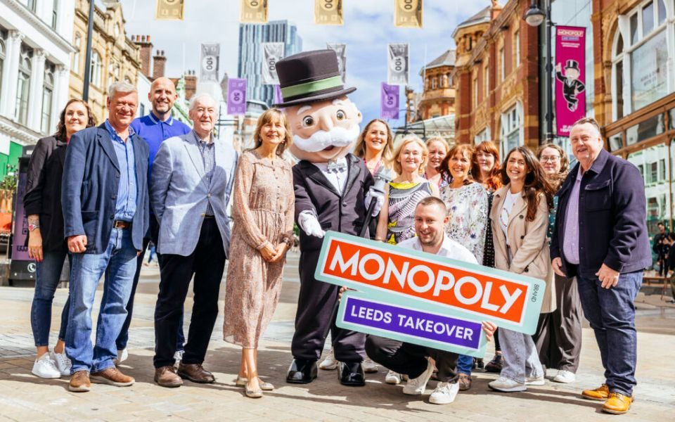 The LeedsBID team standing with a lifesize figure of the Monopoly man, wearing a suit and top hat with a white moustache and monocle, holding a sign reading 'MONOPOLY Leeds Takeover'.
