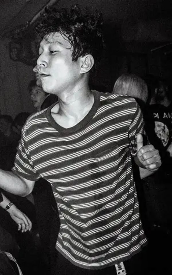 A person with sweaty hair and a striped t-shirt dances in a crowded dancefloor.