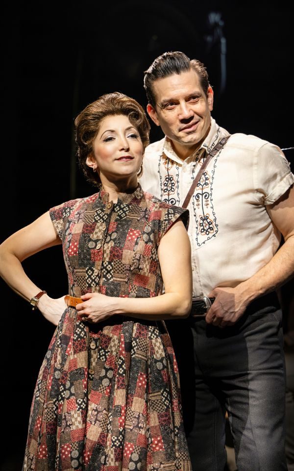 Christina Bianco as June Carter Cash in a printed dress standing next to Christopher Ryan Grant as Johnny Cash in a white country-style top and black leather trousers.