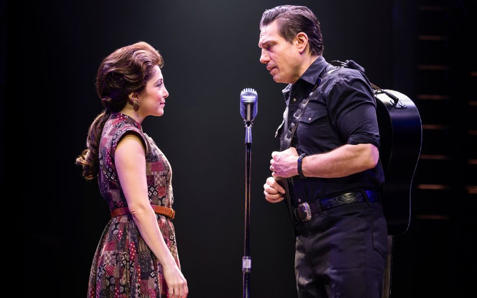 Two actors playing Johnny Cash and June Carter stand either side of a microphone, looking at each other meaningfully.