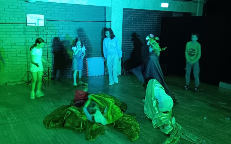 A group of children in a studio setting playing with sheets of fabric beneath a green light.