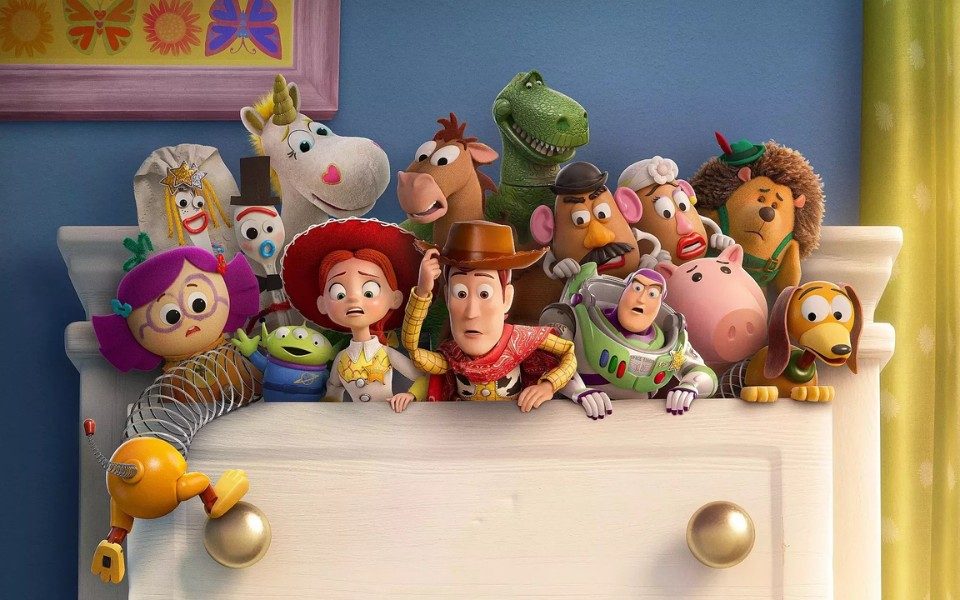A group of animated toys including a cowboy, an astronaut, an alien and a dinosaur all emerge from a white chest of drawers with looks of concern.
