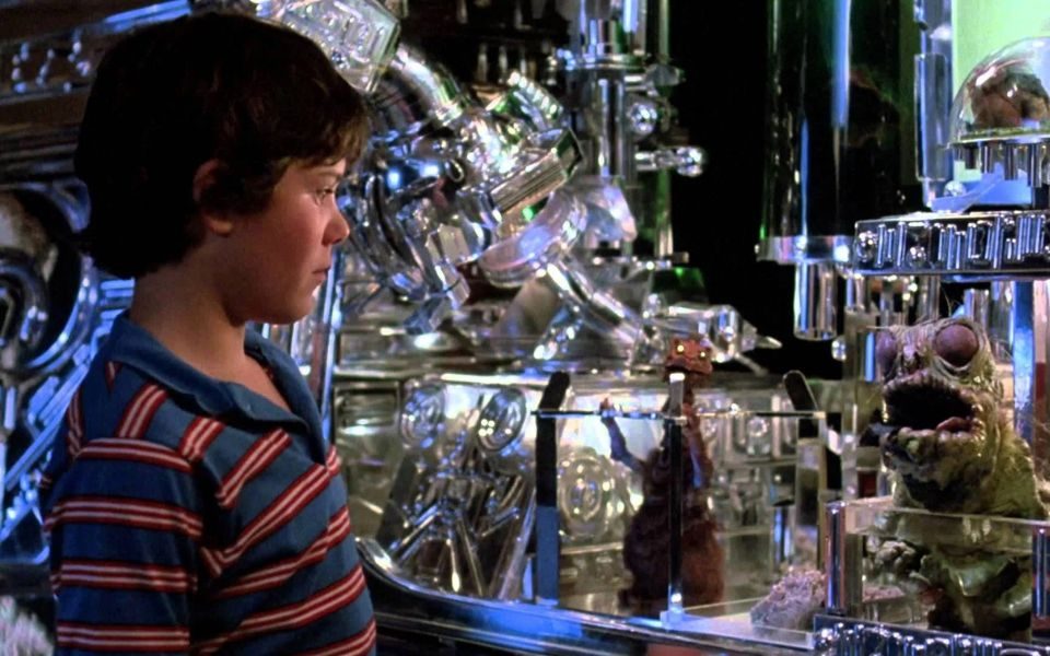 A young boy looks at a series of shiny chrome instruments and two small puppet creatures in glass boxes.