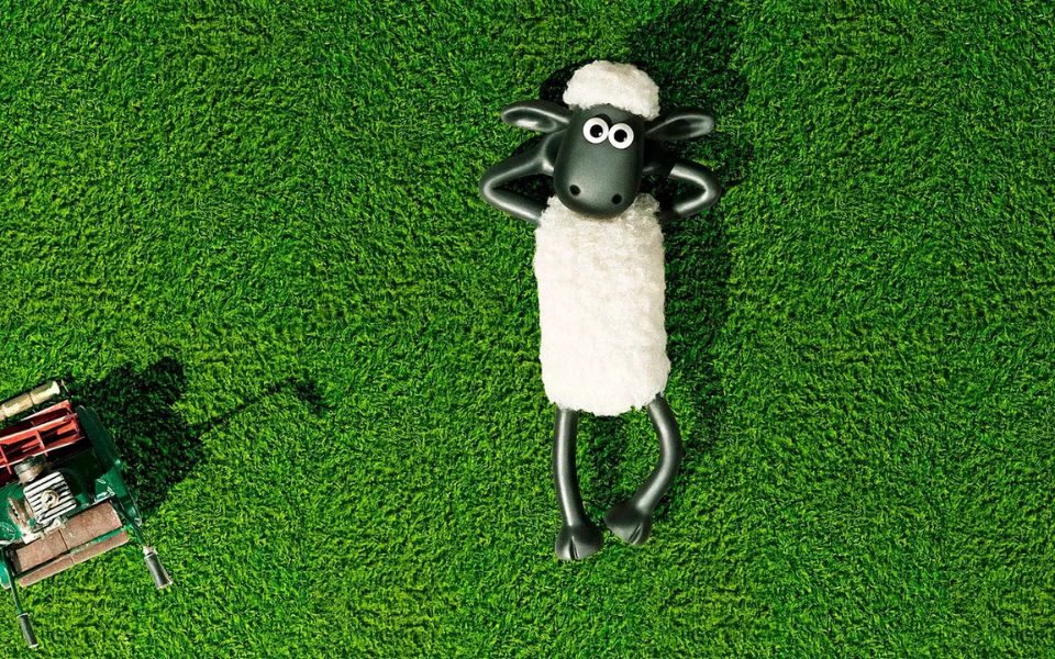 Animated still of Shaun the Sheep lying on a bed of vibrant green grass.