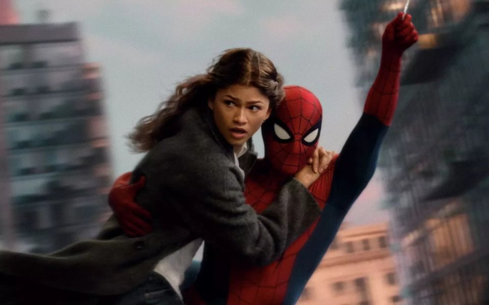 Spiderman swings through the city on a web in a red and blue suit, as a woman in an overcoat (MJ) clings to him. Skyscrapers blur in the background.