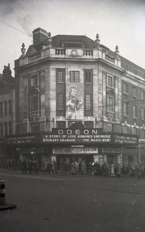 Black and white archive image of the Odeon theatre at the corner of a busy street. Below the neon sign, text reads: A story of love, romance and music. Stewart Granger. 'The Magic Bow.'