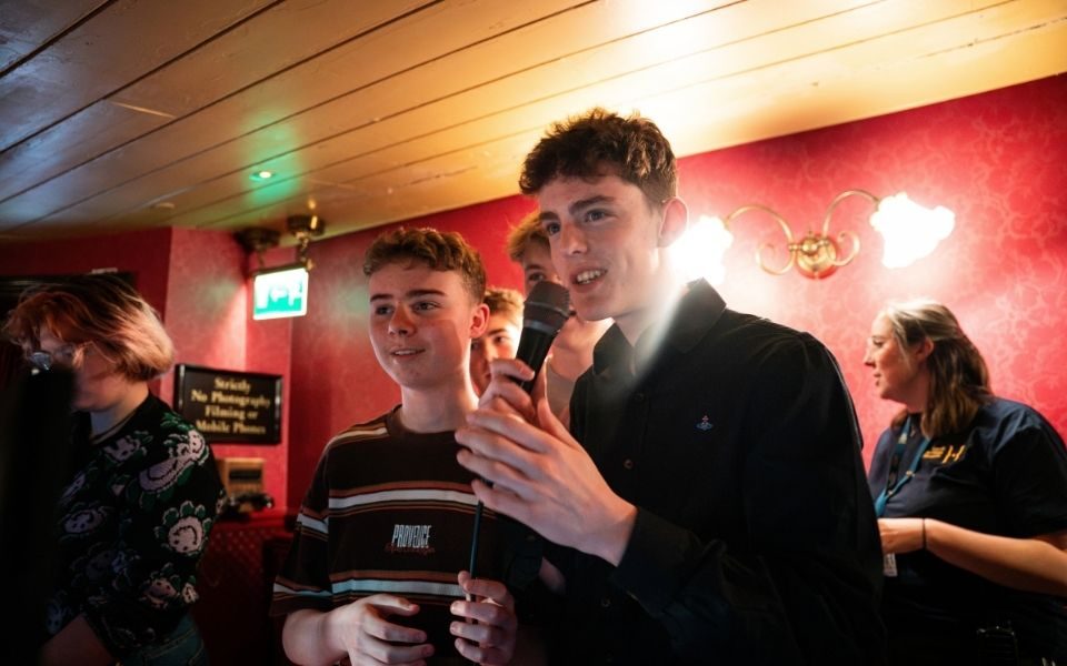 In the technical booth at City Varieties Music Hall, students stand together, with a student in the foreground speaking into a microphone.