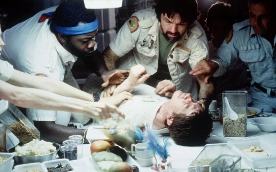 A group of people hold down another person on a dinner table.