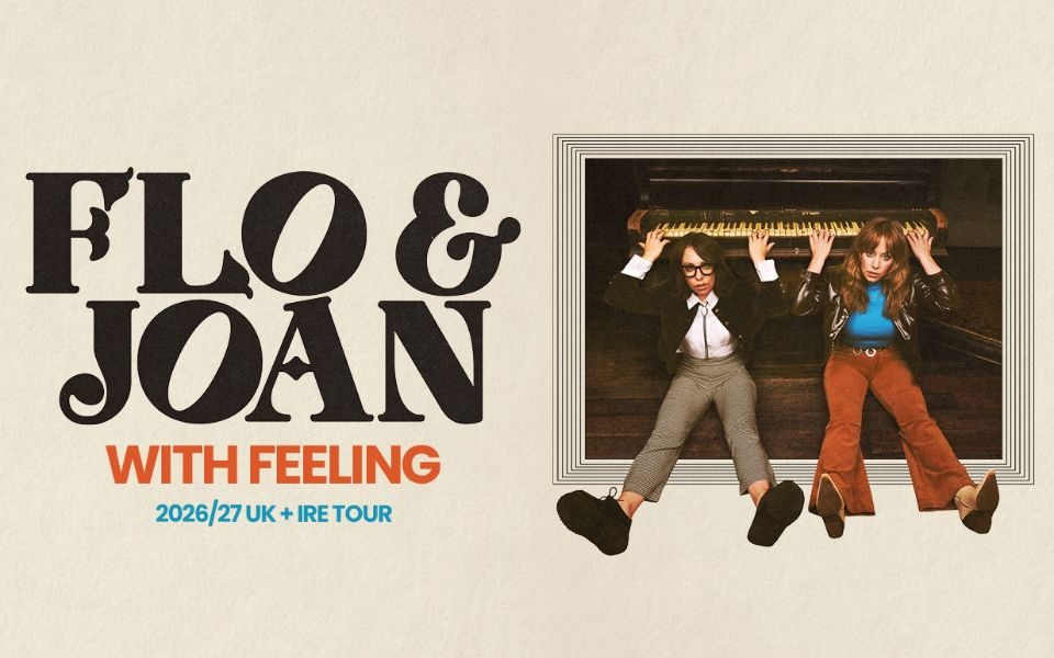 Inside a picture frame, Flo and Joan sit on the floor with their legs extended, and their arms playing a piano positioned behind their heads. Bold text reads: Flo & Joan: With Feeling. 2026/27 UK + IRE tour.
