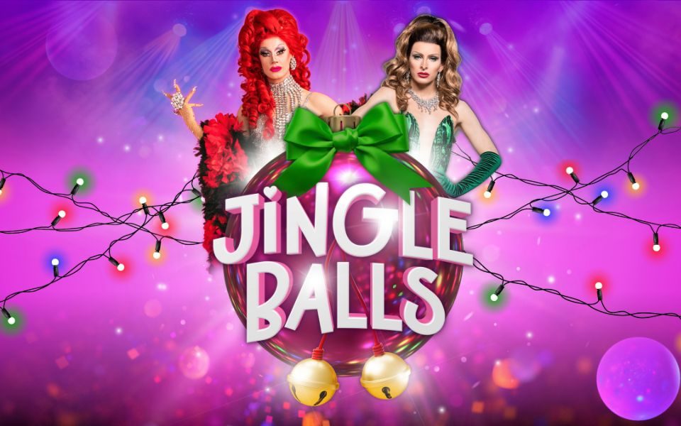 Divina de Campo and Veronica Green pose in sequined outfits and extravagant wigs behind a large pink bauble with a green bow and golden bells. Fairy lights are across the pink and purple background. Text reads: Jingle Balls.