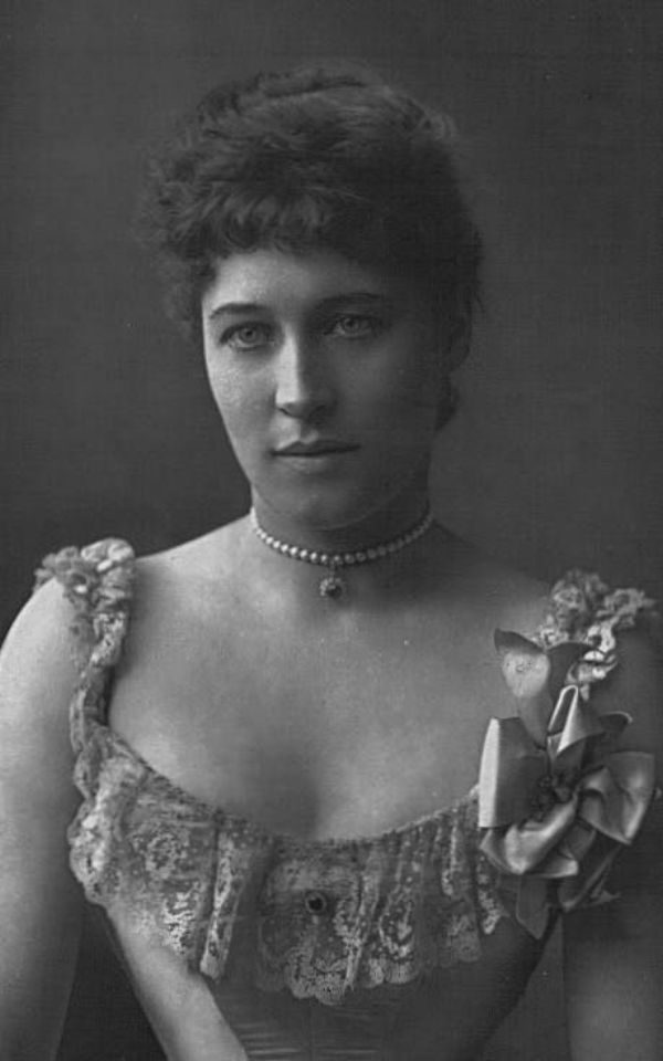 A black and white image of a woman in a corset wearing a pearl necklace