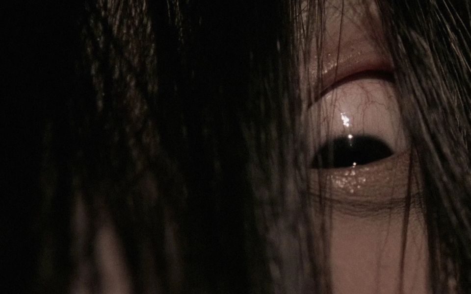 A close-up shot of an eye revealed from between strands of hair. The iris is half covered by the eyelid in an unnatural expression.