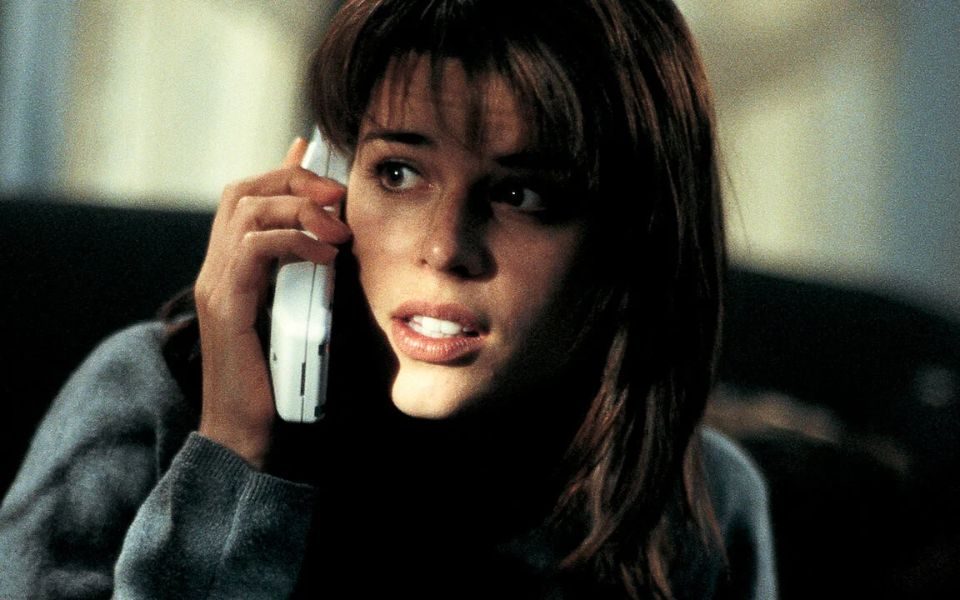 A woman in a dimly-lit room answer the phone, glancing at something off-camera.
