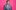 Wearing a grey suit in front of a pink background, Stephen K Amos stands laughing.