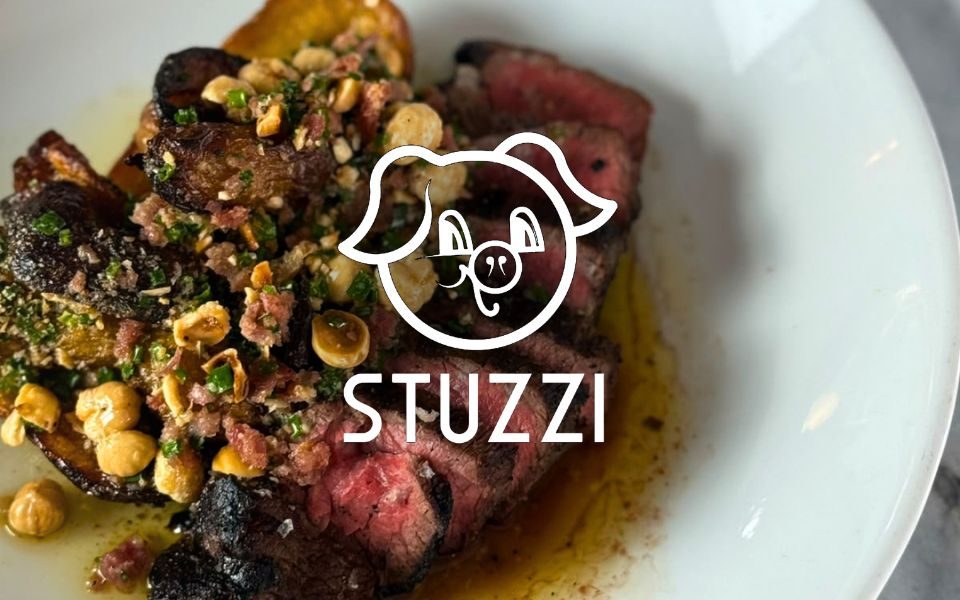 The Stuzzi logo, featuring a pig, over an image of a sliced rare steak garnished with crispy potatoes, nuts and herbs.