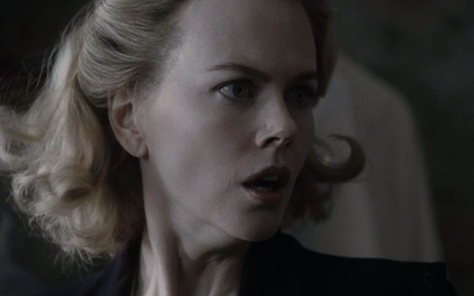 Dimly-lit and in low saturation, a woman dramatically turns her head as if gasping.