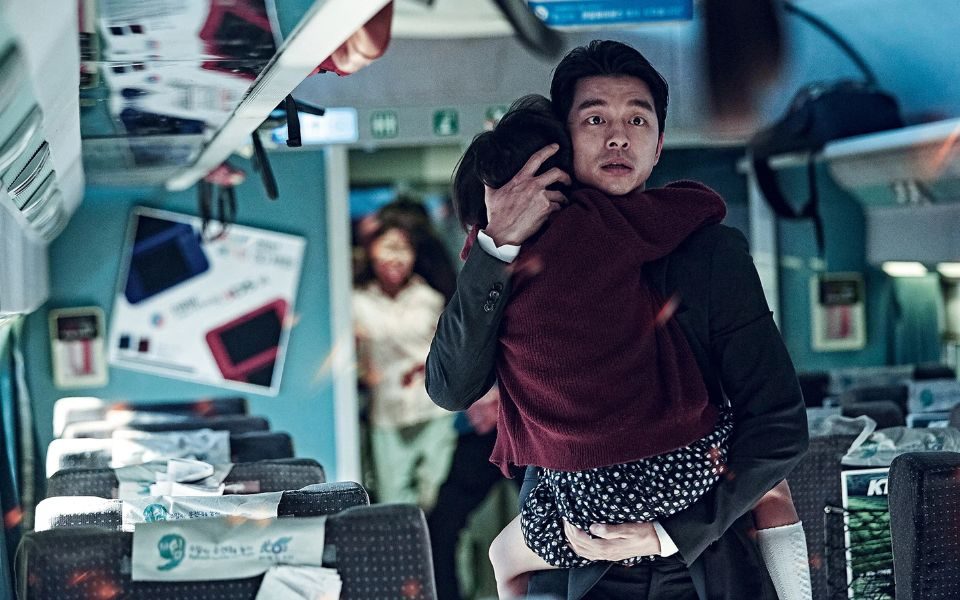 On a train, a man holds a young girl and looks ahead in distress.