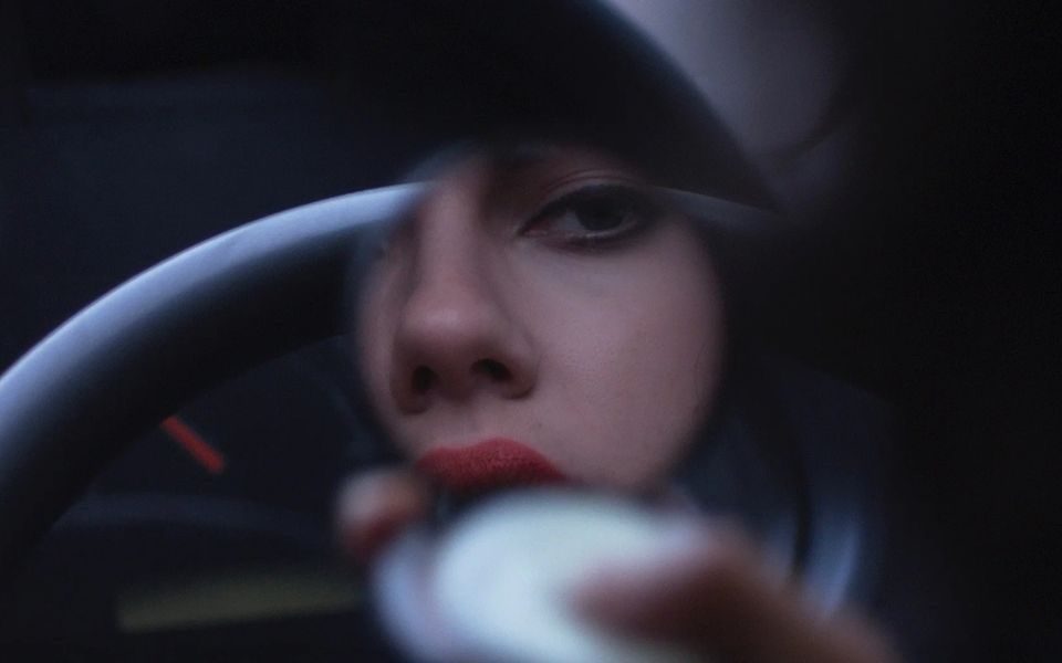 A woman wearing red lipstick looks at herself in a circular compact mirror.